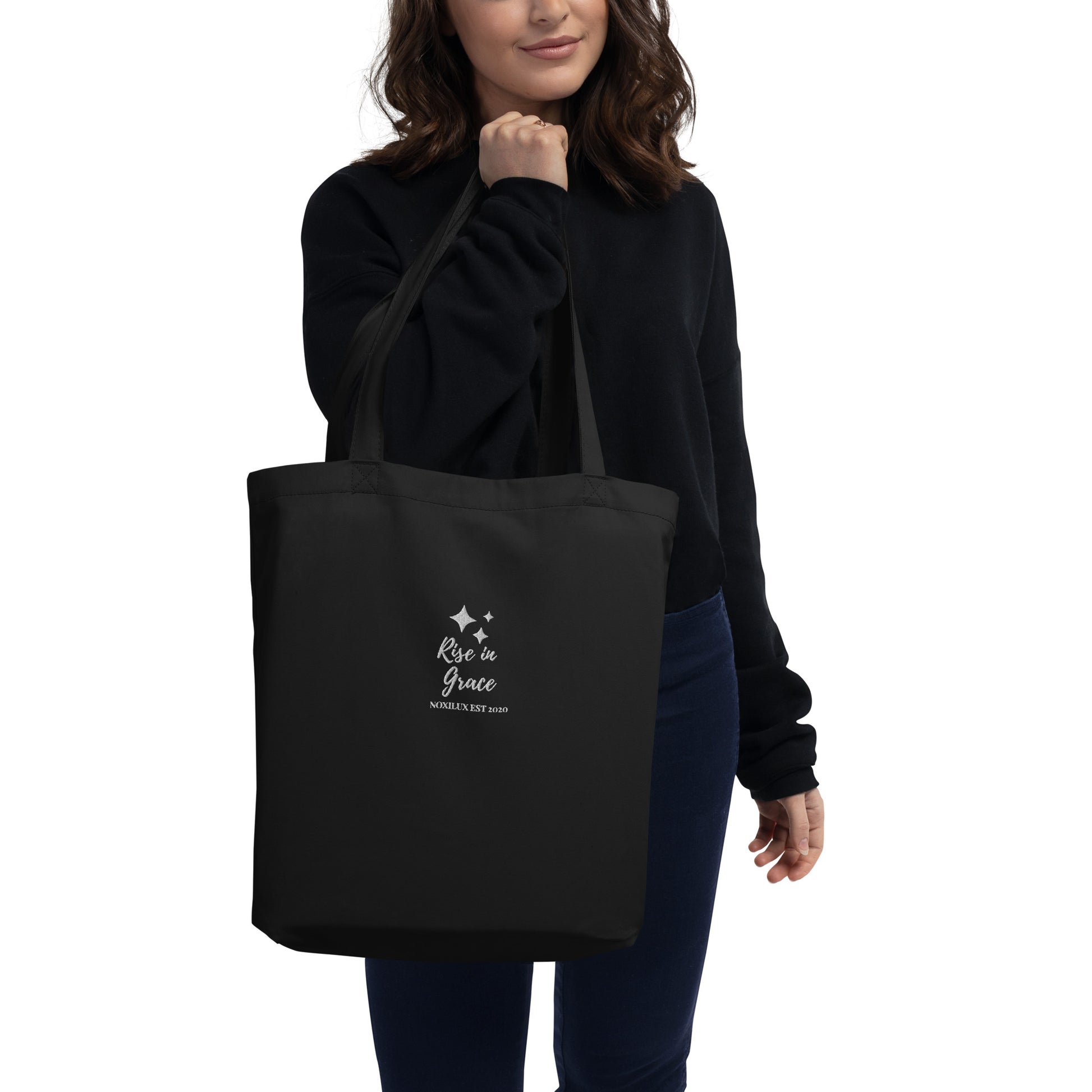 Black shopping tote bag with 'rise in grace.' text and a sparkle symbol on a white embroidered. Eco-friendly organic cotton.